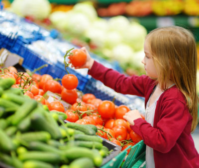 Little girl choosing tomatoes in a food store or a supermarket
